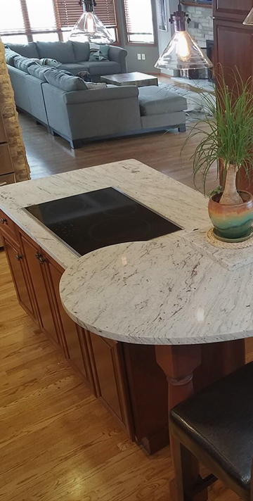 Curved granite island countertop with a built-in cooktop and cherry cabinets open to the living room