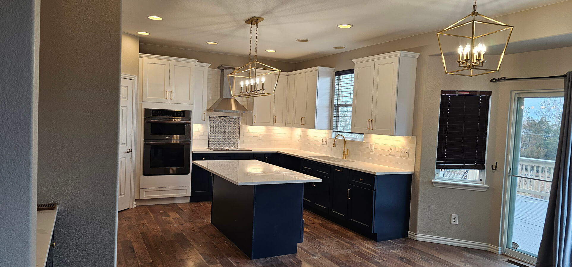 White perimeter cabinets and a navy island with brass pendants and double wall ovens in a Denver kitchen