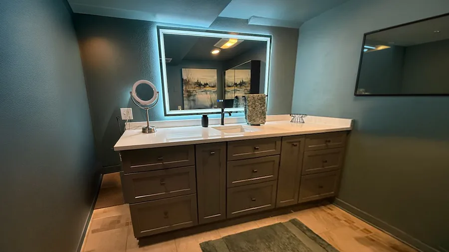 Bathroom vanity with a backlit LED mirror, espresso cabinetry and a white quartz countertop