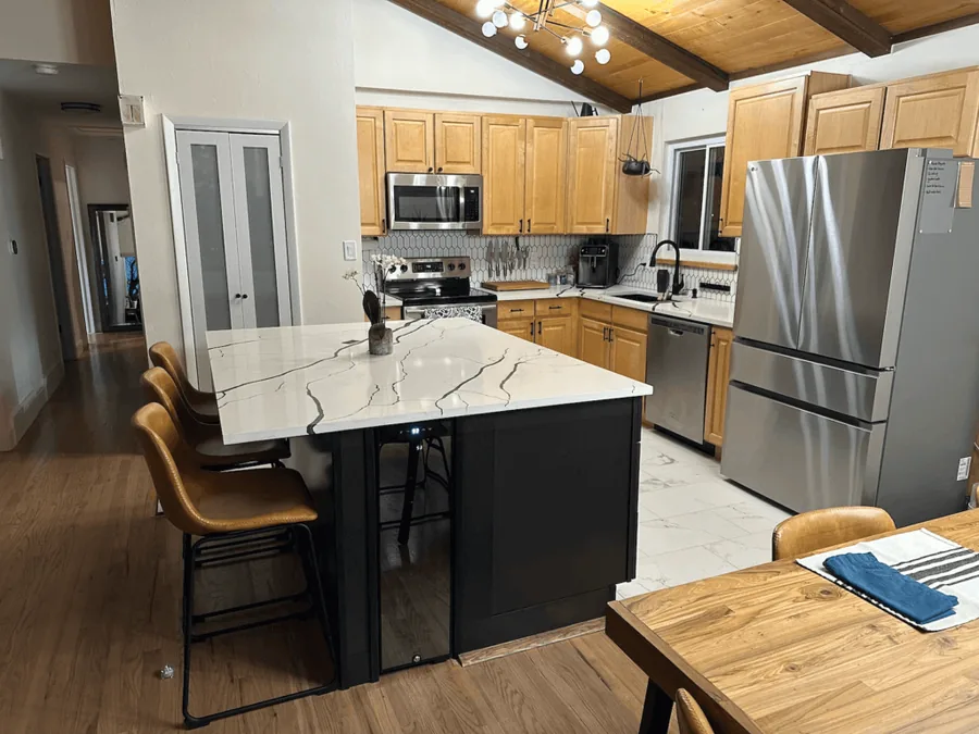 Black island with a veined quartz countertop against light wood cabinets