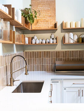 Kitchen coffee bar with open wood shelving, terracotta tile backsplash, undermount sink, and brushed brass pull-down faucet