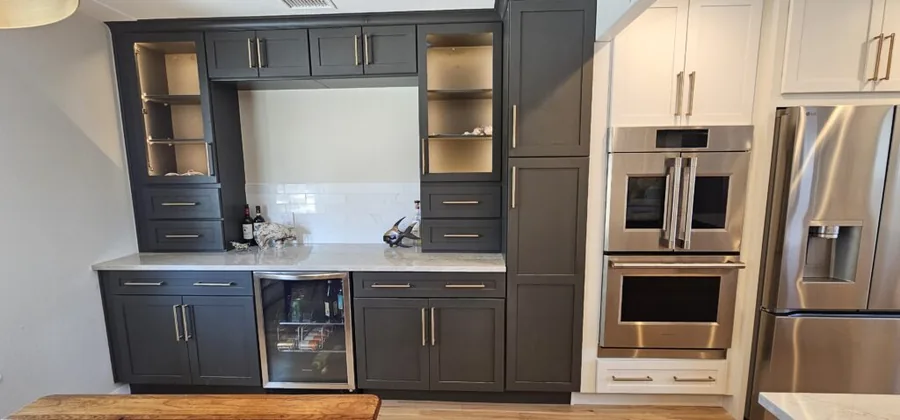 Dark gray coffee bar cabinetry with glass uppers beside stainless wall ovens