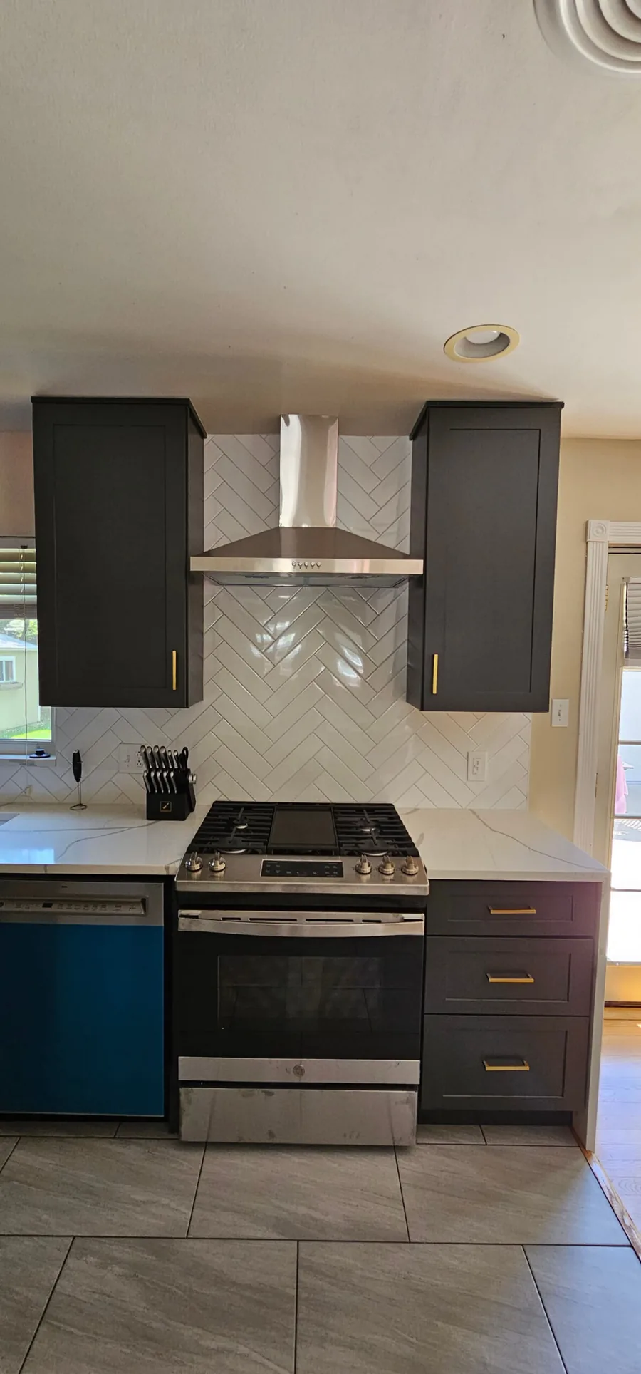 Dark gray cabinets with a herringbone tile backsplash and a stainless range