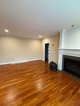 Empty living room with refinished hardwood floors, white fireplace mantel, and crown molding before remodeling
