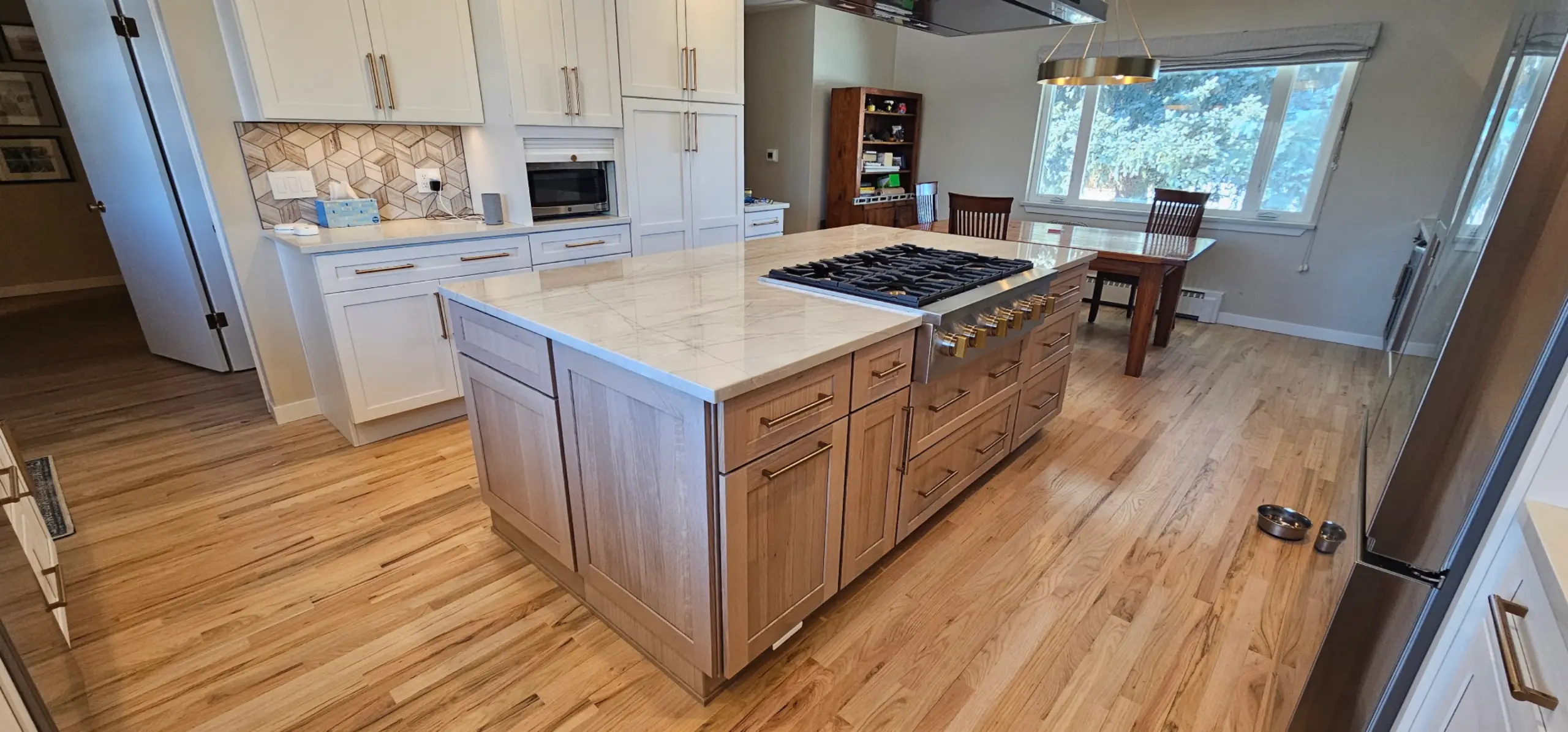 Kitchen with wide-plank hardwood flooring, oak cabinetry and a gas cooktop island with wooden barstools
