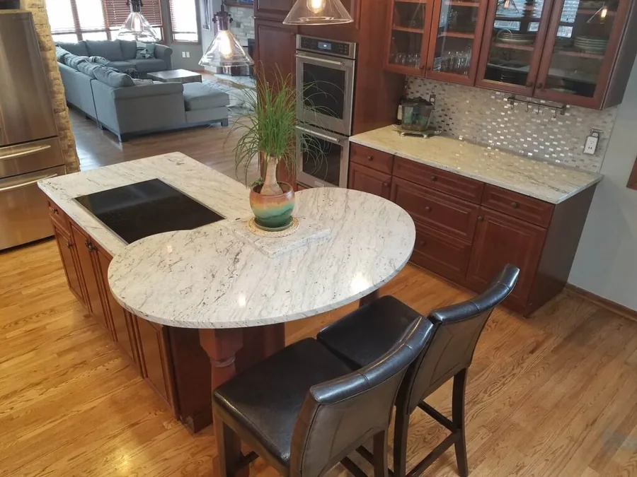Curved granite island with bar seating and double wall ovens in a cherry cabinet kitchen