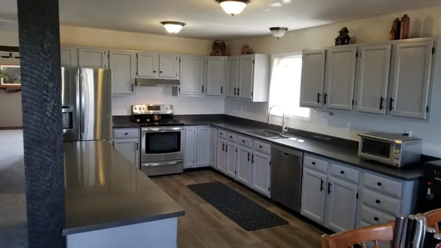 Gray cabinet kitchen with a stainless range and dishwasher against dark countertops