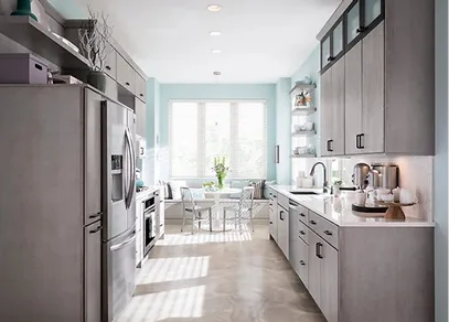 Grey and taupe frameless kitchen cabinets with a stainless refrigerator and a bright breakfast nook