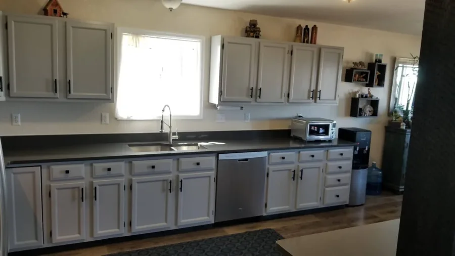 Gray kitchen cabinets with a window above the sink and dark countertops