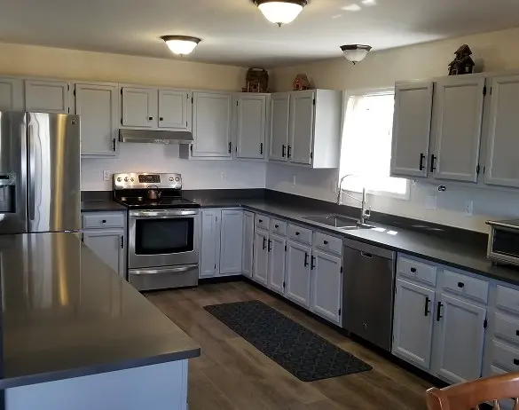 Updated kitchen with dark gray countertops, painted white cabinets with black hardware, stainless steel appliances, and wood-look flooring
