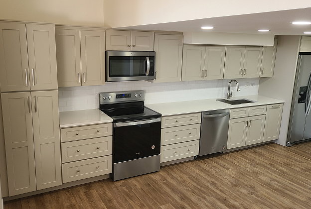 Greige shaker kitchen with white stone countertops, stainless range, microwave and refrigerator on wood-look flooring