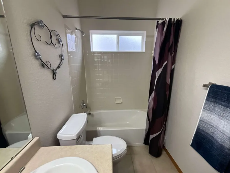 Hall bathroom before remodeling, with a dated tub, shower curtain and beige fixtures