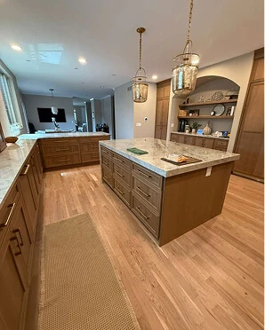 Light oak kitchen island with granite countertop, lantern pendant lights, and built-in arched shelving over hardwood floors
