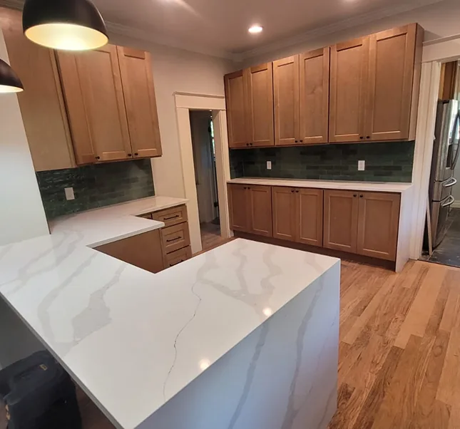 Maple shaker kitchen cabinets with waterfall quartz peninsula, green tile backsplash, and hardwood floors
