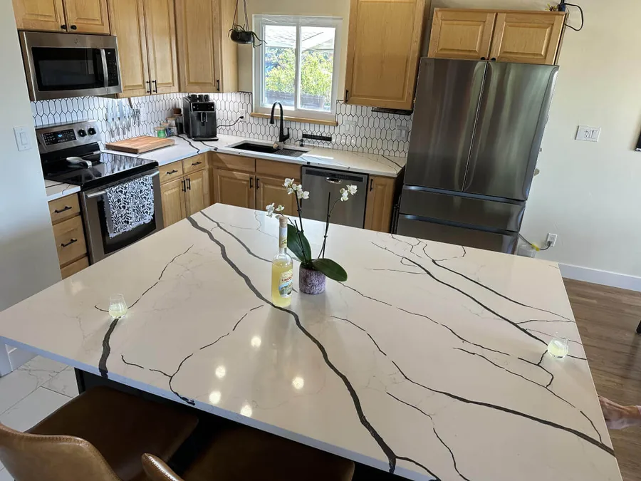 Marble-look quartz waterfall island in a light wood cabinet kitchen