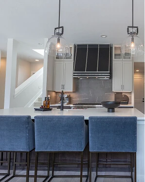Modern kitchen island with blue velvet barstools, black custom range hood, marble backsplash, and glass globe pendant lights