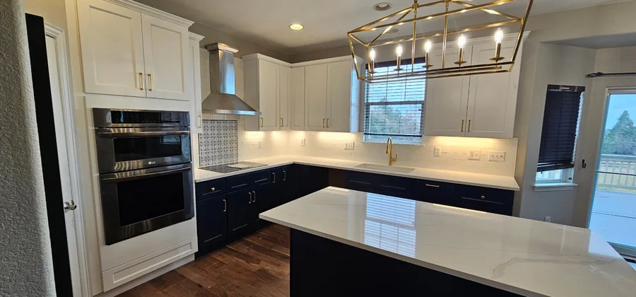 Navy lower cabinets with white uppers, gold pendants and stainless wall ovens