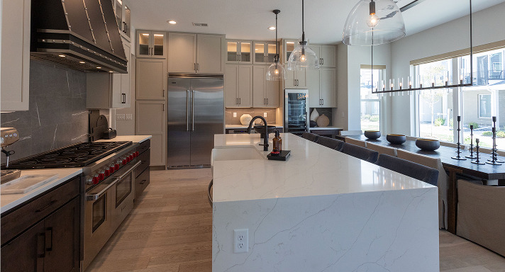 Open-concept kitchen with a white waterfall-edge stone island, dark backsplash, professional gas range and stainless refrigerator
