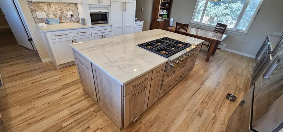 Quartz-topped wood island with a gas cooktop in a white cabinet kitchen