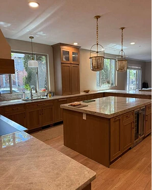 Traditional oak kitchen with granite countertops, large center island with beverage fridge, and lantern pendants above a window-lined perimeter
