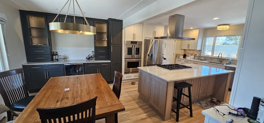 Two-tone kitchen with a dining table, island cooktop and stainless range hood