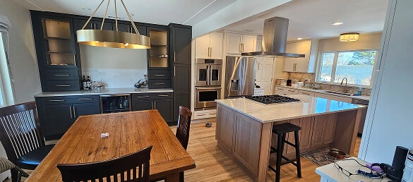 Two-tone kitchen remodel with navy and white cabinets, quartz island with gas cooktop, stainless hood, and wood dining table