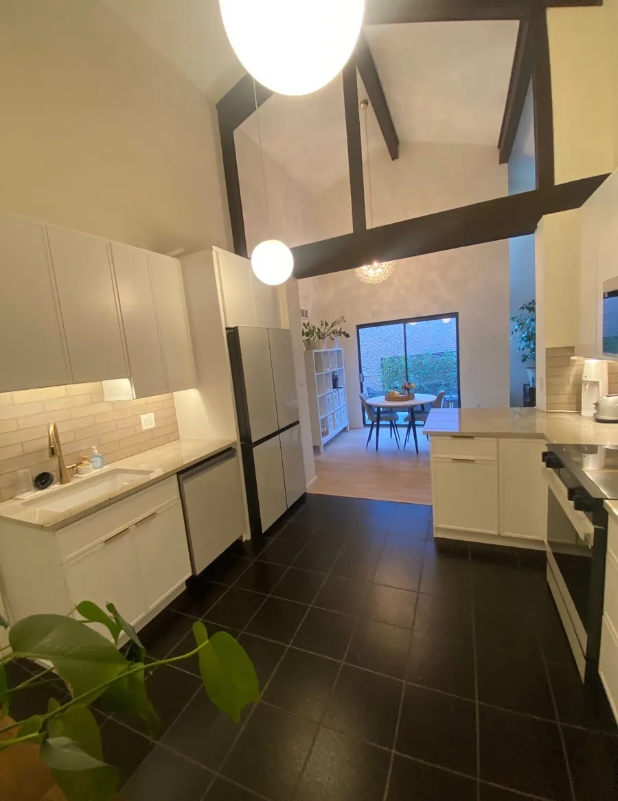 White kitchen remodel under a vaulted ceiling with exposed beams and dark tile flooring