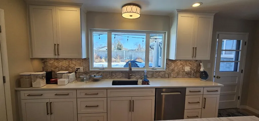 White kitchen cabinets with a tile backsplash and a window above the sink