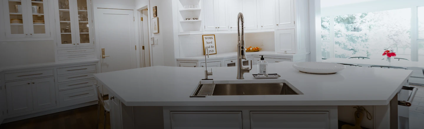 White transitional kitchen with a large quartz island, undermount stainless steel sink, and glass-front cabinetry