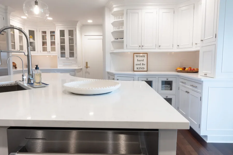 White quartz island with a prep sink and glass-front display cabinets