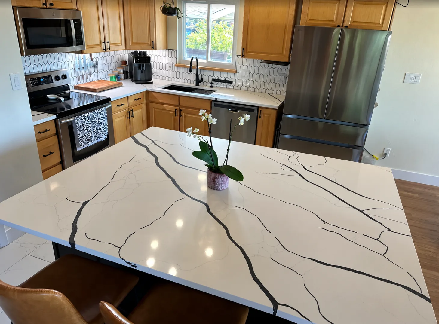 White quartz kitchen island countertop with bold black veining, with oak cabinets, a white picket tile backsplash and stainless steel appliances behind it