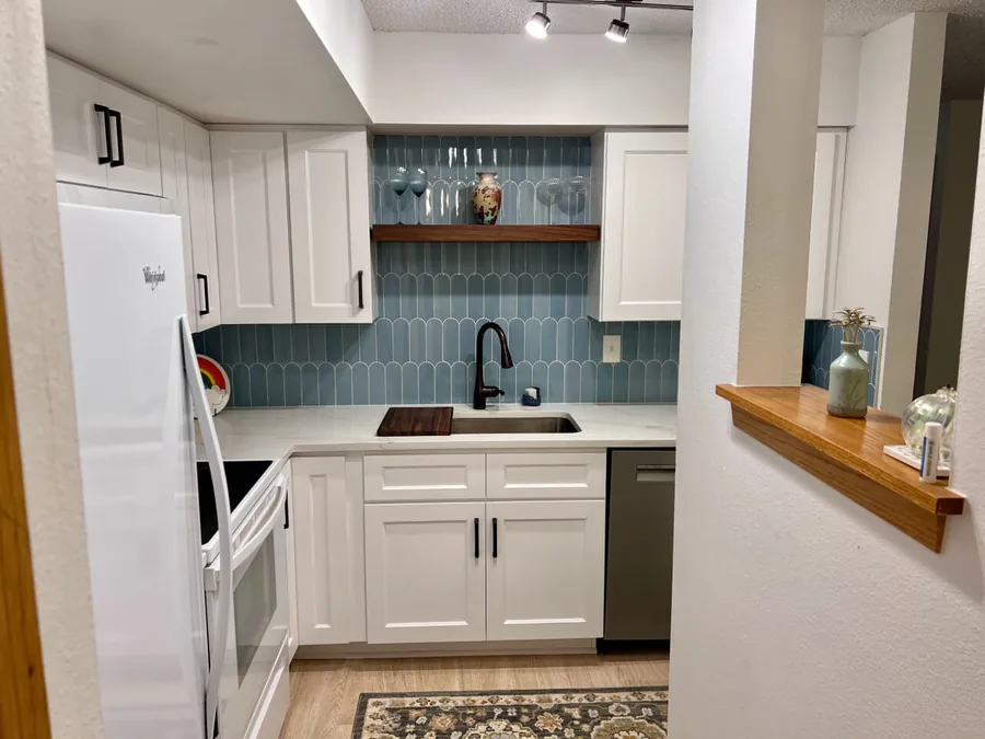 White shaker cabinets with a blue tile backsplash and an open wood shelf