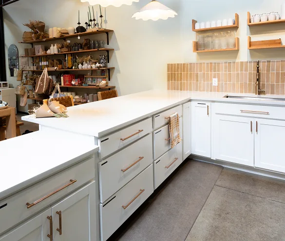 White shaker cabinets with quartz island, terracotta tile backsplash, and brass hardware in a retail kitchen space