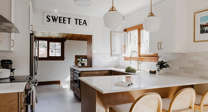 White shaker kitchen with a stone breakfast bar, cane-back counter stools and globe pendant lights