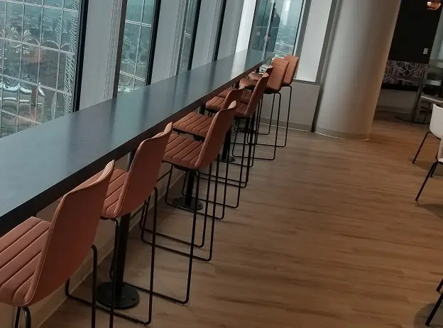 Long dark stone window counter with tan leather bar stools overlooking a city view, set on light wood flooring in a modern lounge space